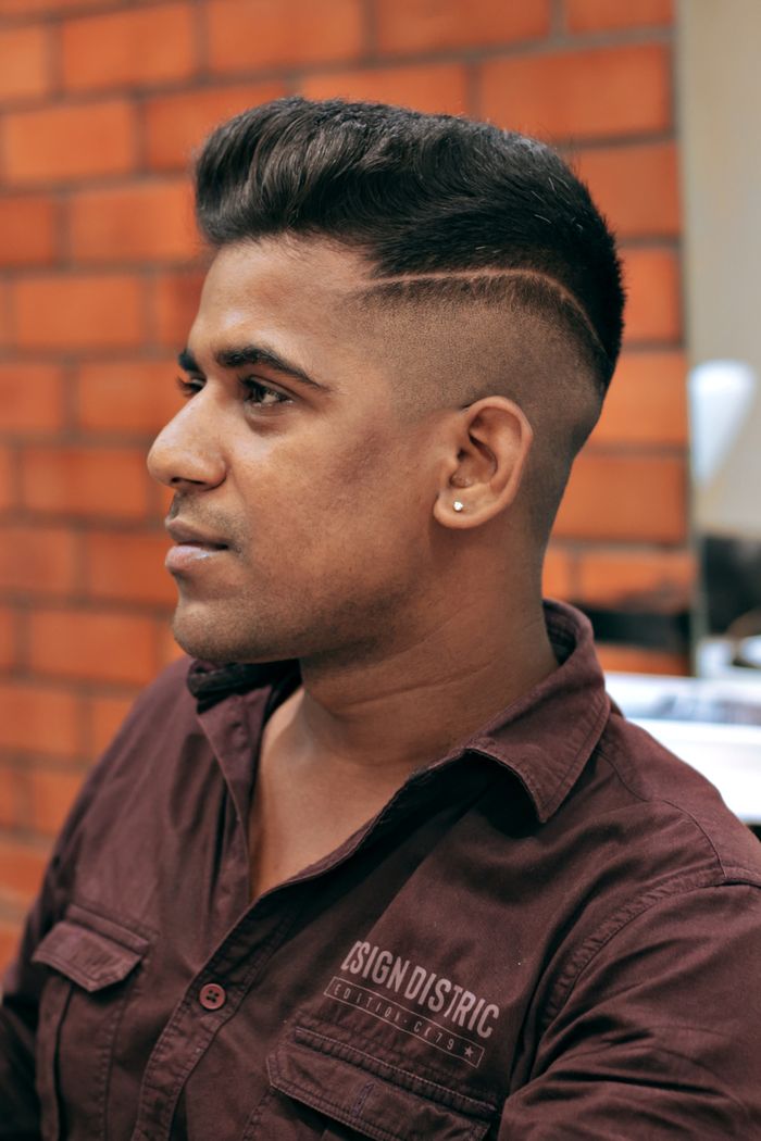 Profile view of a stylish South Asian man showcasing a modern haircut in a barbershop setting.
