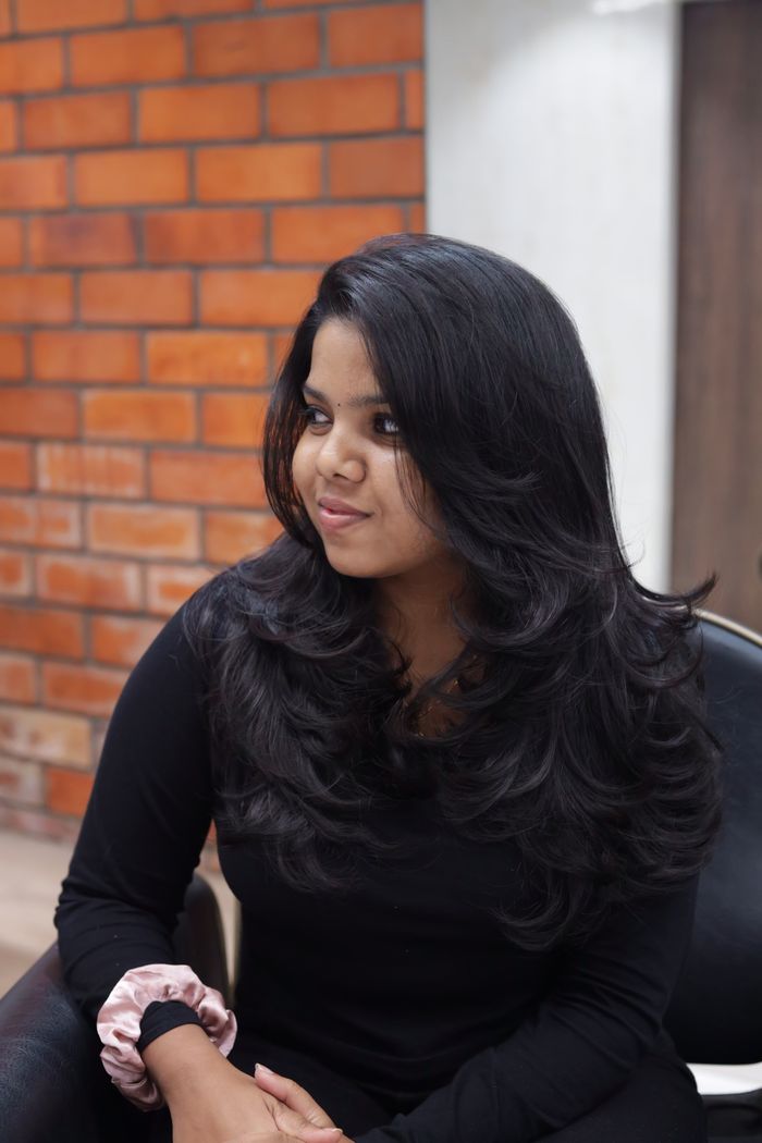 why-choose-us Stylish portrait of a woman with long black hair in a black outfit sitting indoors.
