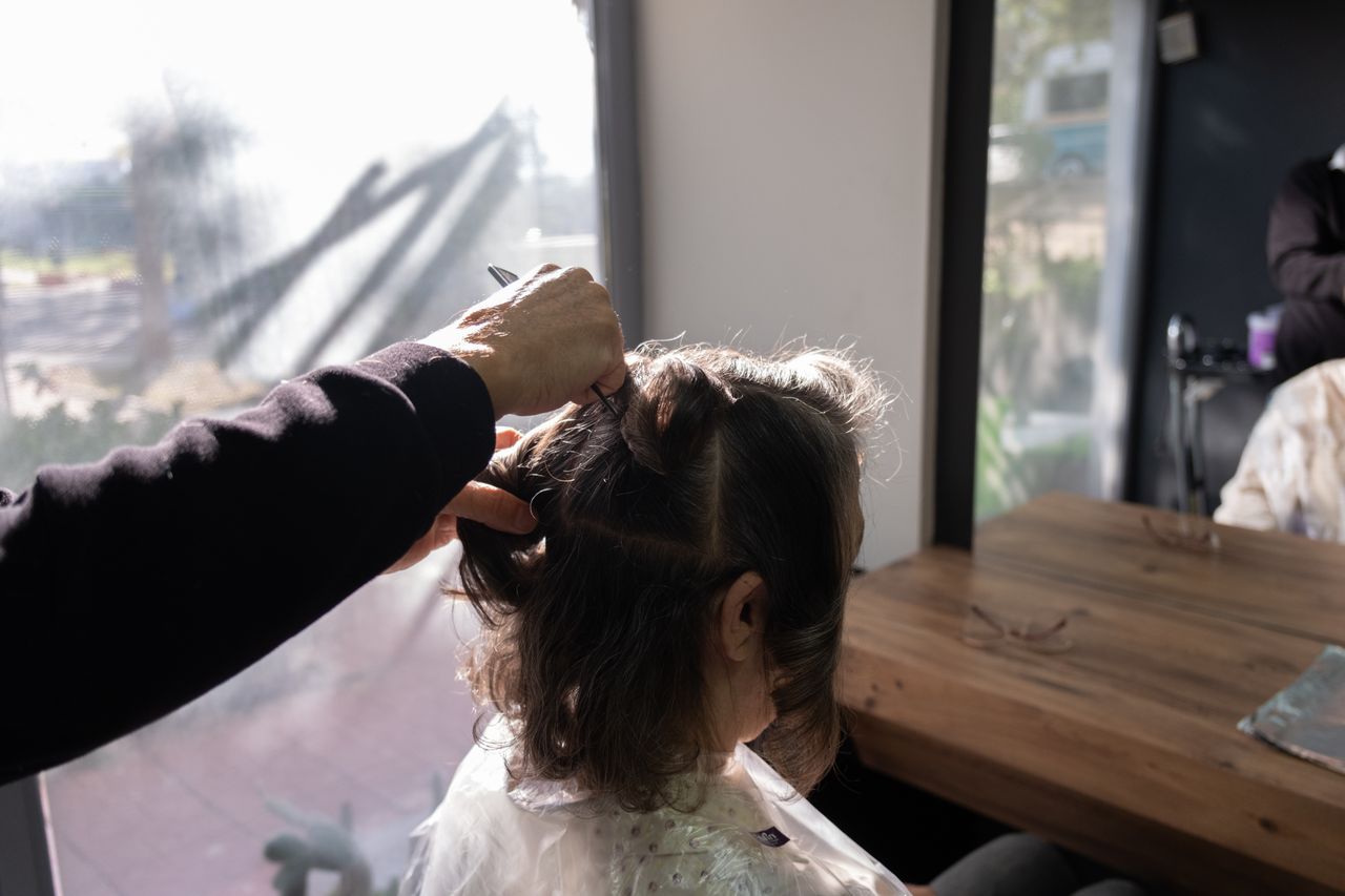 services-03 A hairdresser trims a client's hair in a sunlit salon in İzmir, offering a cozy and professional atmosphere.
